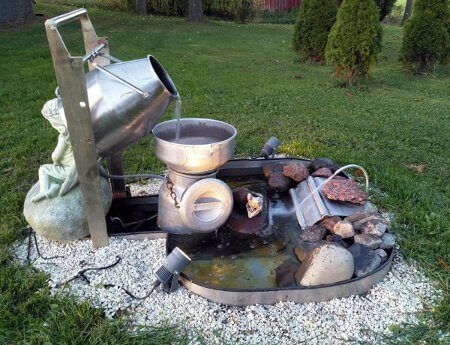 Suihkulähde, jossa vesi valuu kannulypsykoneen kannusta maitotonkkaan siivilän läpi