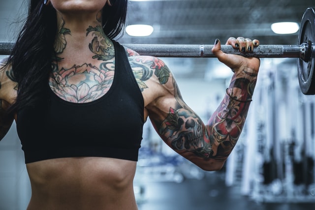Close up of tattooed strong woman carrying barbell