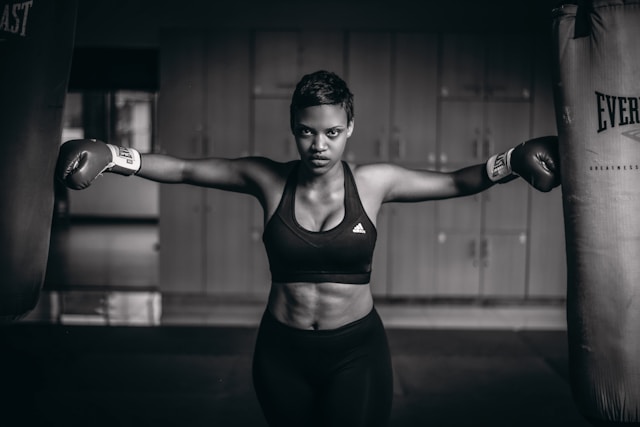 Grayscale photo of boxer woman with boxer glowes touching boxer bags